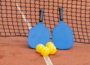 Two pickleball paddles and three balls resting on an outdoor court