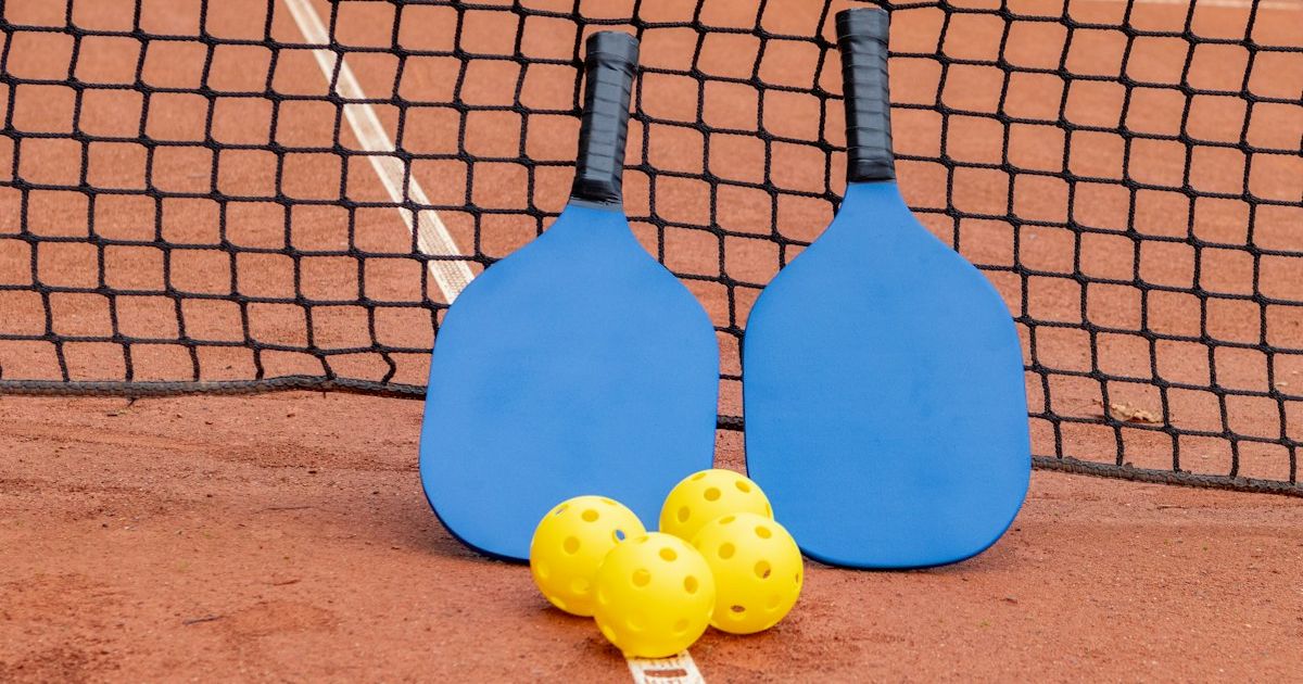 Two pickleball paddles and three balls resting on an outdoor court