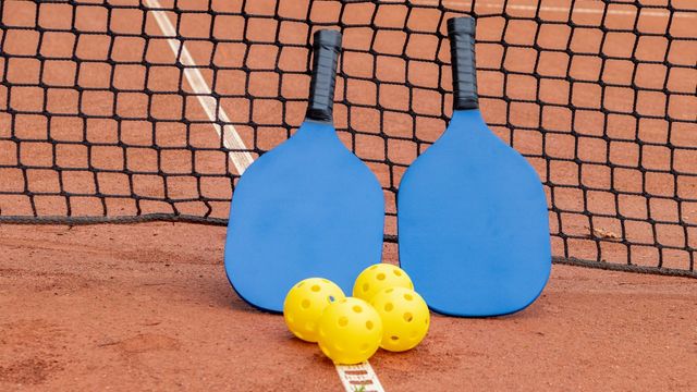 Two pickleball paddles and three balls resting on an outdoor court